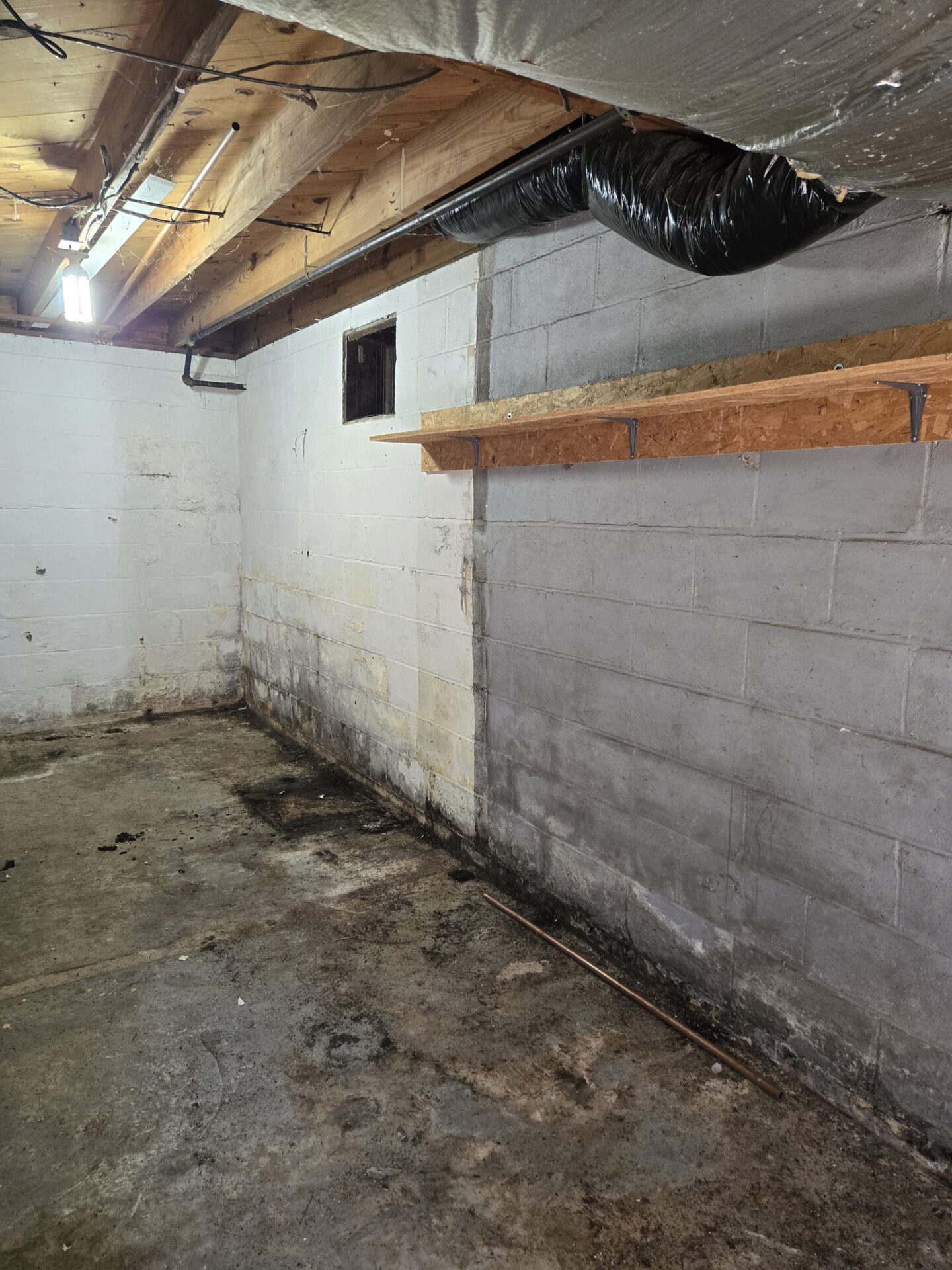 A basement corner with ductwork, exposed joists, and signs of dampness on walls